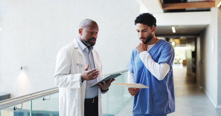 Doctor, tablet or nurse with folder discussion in clinic for treatment solution, opinion or advice. Health team, men or medical records in hospital hallway for explaining results or report comparisonの写真素材