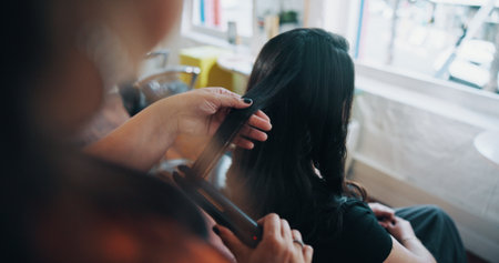 Hands, hairstylist and flat iron with woman in salon for cosmetology, beauty and grooming. Hairdresser, parlor and customer makeover with people in store for hair care, relax and straightenerの写真素材