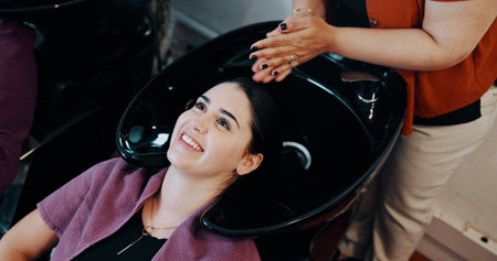 Hairdresser, customer or women at washing basin at beauty salon, professional service or cleaning scalp. Smile, shampoo treatment or people with stylist for hair care routine, grooming or high angleの写真素材