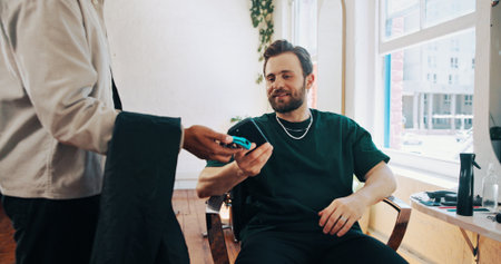 Happy man, hairdresser or customer paying with phone for payment, banking or pos machine in salon. Male people, barber or client with mobile smartphone for NFC tap or wireless transaction in parlorの写真素材