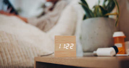 Digital alarm, clock or bedroom in home for sleeping schedule, person and rest for wellness. Electronics, watch and LED display with time for reminder, ui or pills on pedestal for health at apartmentの写真素材