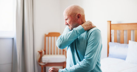 Senior man, bed and shoulder with pain for fibromyalgia, muscle tension or strain in old age home. Elderly, male person or sore neck with pressure for arthritis, tendinitis or joint inflammationの写真素材