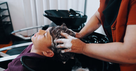 Hairdresser, customer or boy with washing at basin in salon, professional service or cleaning scalp. Child, shampoo treatment or people with stylist for hair care routine, head massage or high angleの写真素材