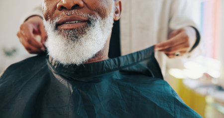 Barber, hands and customer beard with cape for grooming service, start makeover and styling appointment. People, mature client and consultation in salon with facial hair trim, cover and preparation.の写真素材