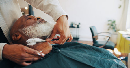 Shave, barber and man with customer in chair for grooming, haircut and trim for beard service. Hair salon, appointment and people with razor for styling, wellness and hairdresser in barbershopの写真素材