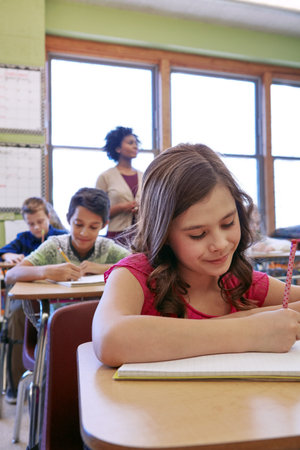 Learning, listening and writing with girl in school classroom for development, future or growth. Book, education and study with happy child student at desk in class for knowledge, lecture or lessonの写真素材