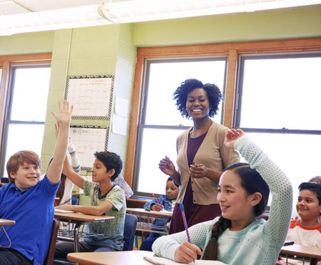 Happy, teacher and children with hands up, classroom and students with academic growth or education. Elementary school, woman and kids with answer, knowledge and cognitive development with lessonの写真素材