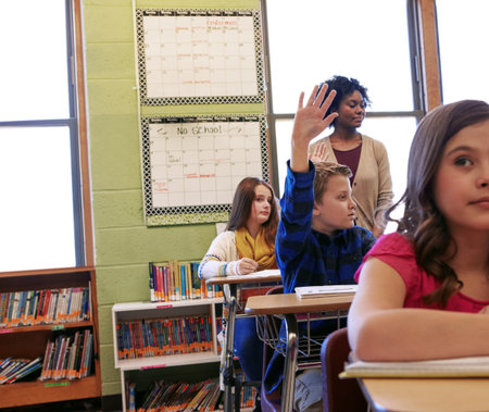Classroom, children and hand up for answer, education and students with academic growth or learning. Elementary school, teacher and boy with gesture for question, knowledge and cognitive developmentの写真素材