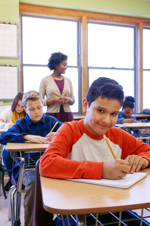 Portrait, happy boy and writing in classroom with pencil for knowledge, education or assignment....