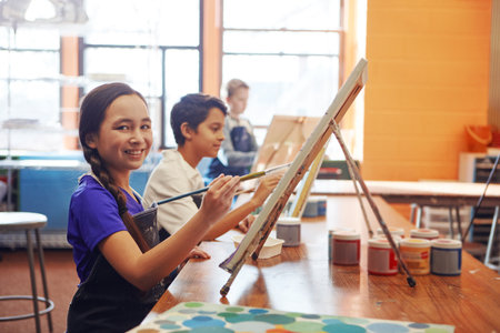 Portrait, painting or girl with smile for class, creative creation or fine motor skill development in art. Education, artistic learning or happy students with canvas for lesson, paint brush and childの写真素材
