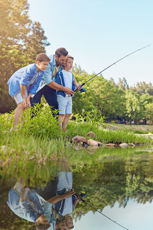 Fishing, dad and bonding with children, lake and teaching son with rod on summer vacation or outing. Outdoor, man and kids with equipment to catch sea creatures, parent and family in nature and tripの写真素材