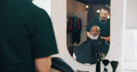 Haircut, mirror and man in salon with preparation, cover or hair removal in small business. Grooming, reflection or hairdresser in studio with cape, trim routine or customer styling in beauty startupの写真素材