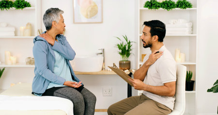 Consultation, physical therapist and mature woman with injury on shoulder, wellness or health. Rehabilitation, chiropractor and person with pain, medical help or assessment with clipboard in clinicの写真素材