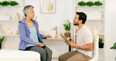 Consultation, mature woman and physiotherapist in office for health, wellness or medical advice. Smile, person and physical therapist in clinic for healing, chiropractor and help with clipboardの写真素材