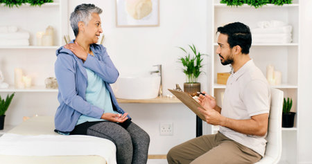 Consultation, mature woman and physical therapist in office for health, wellness or shoulder injury. Rehabilitation, person and physiotherapist with chiropractor, medical help or diagnosis clipboardの写真素材
