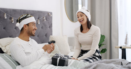 Christmas, love or couple in bed with gift box, romantic moment or gratitude on xmas morning. Festive, man and woman in house with present, healthy relationship or appreciation in holiday traditionの写真素材