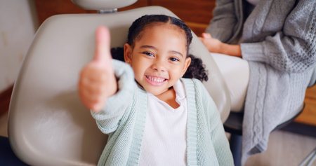 Portrait, smile and thumbs up with girl at dentist for optometry goals, success or support. Emoji, hand gesture and motivation with child in chair at dental clinic for healthcare or wellnessの写真素材