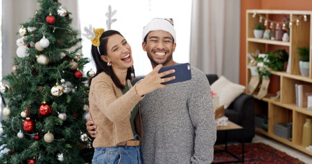 Christmas, couple laugh and selfie with hug in home for holiday memory, social media post or love. Man, woman and profile picture on xmas with embrace for festive celebration, smile and funny partnerの写真素材