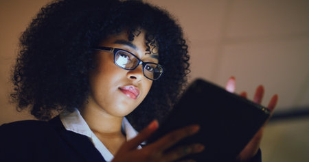 Tablet, reading and businesswoman in office at night with email for investment proposal. Digital technology, communication and female financial manager with finance report for budget from below.の写真素材