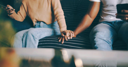 Couple, sofa and holding hands with phone for trust, commitment or relationship together in home. Man, woman or touch with love, care or loyalty on mobile smartphone or couch for weekend in houseの写真素材