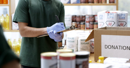 Hands, donation and writing on clipboard for food drive, checklist and boxes at ngo center. Person,...