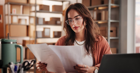 Supply chain, documents and woman with laptop, reading and ecommerce with info. Person, shipping schedule and entrepreneur with paperwork, inventory and checklist for delivery bill or business ownerの写真素材