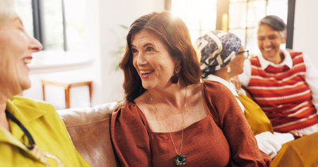 Happy, friends and old women on couch, home and bonding with gossip in lounge, laughing and reunion. Senior people, conversation and humor for funny joke in living room, flare and break in apartmentの写真素材