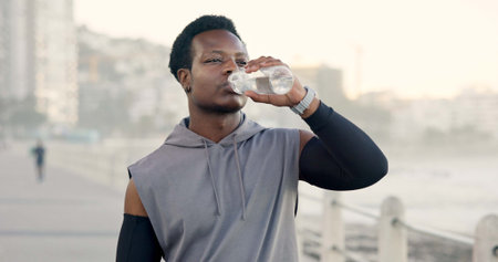 Man, fitness and drinking water at beach on promenade, break and outdoor with hydration for...
