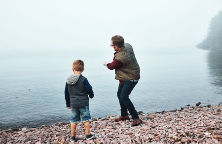 Father, kid and throw stone by river with connection, game and bonding together on weekend getaway....