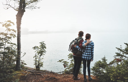 Couple, hug and sightseeing with ocean for hiking journey, adventure or travel together. Back view,...