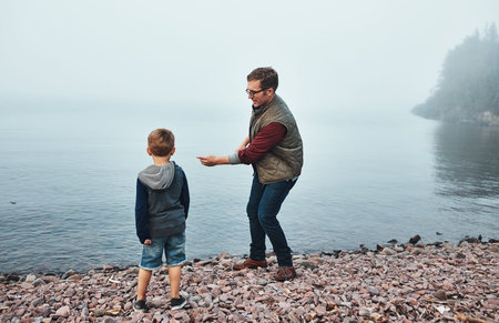Father, son and throw stone by river with connection, game and bonding together on weekend getaway....