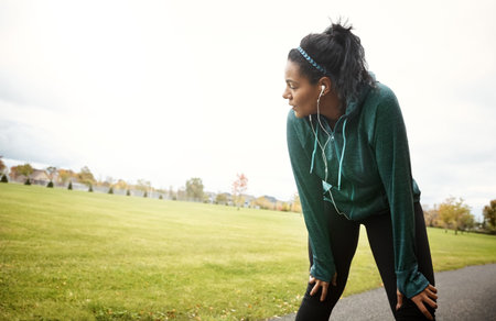 Runner, woman and rest in park with earphones, stop cardio workout and listening to music for...
