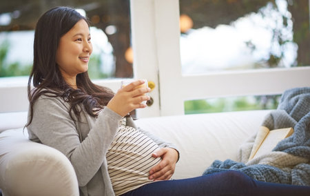 Pregnant, woman and thinking on couch with tea, touch stomach or vision for motherhood on weekend....
