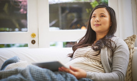 Tablet, relax and thinking with pregnant woman on sofa for baby research, prenatal care app and...
