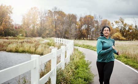Runner, woman and smile with exercise, park and fitness routine with music for jog in nature....