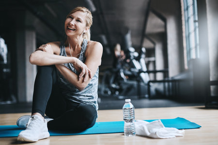 Fitness, music and woman on yoga mat in gym, wellness and thinking on break with laugh. Exercise...