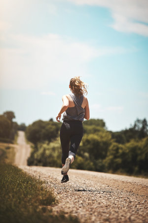Back, woman and runner with road, training and exercise routine with nature for jog outdoor....