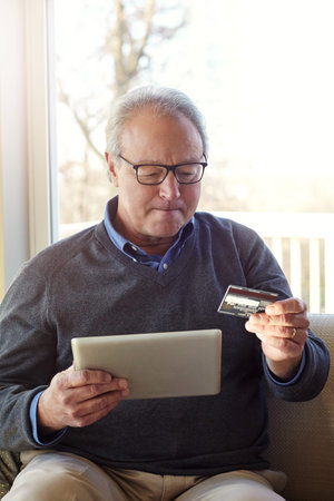 Senior man, tablet and credit card on couch for e commerce in lounge with glasses, discount or deal...