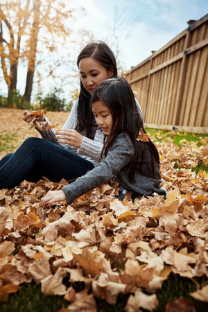 Girl, mother and together with leaves in backyard, autumn lawn and family for vacation with...
