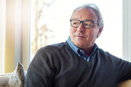 Glasses, relax and thinking with old man on sofa in living room of home for reflection or wellness....