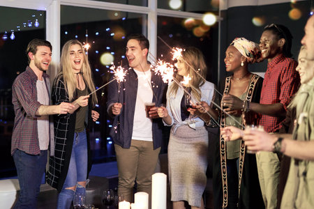 Laughing, friends and group with sparklers, party and happy with alcohol or celebration for new...