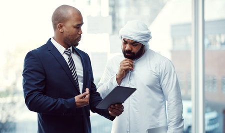 Meeting, partnership and business people on tablet for finance, entrepreneur and review research. Diverse office, teamwork and Muslim man with tech for budget, growth and feedback for proposalの写真素材