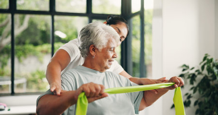 Woman, physiotherapy and senior with resistance band for arm exercise or muscle recovery in clinic. Female person, physio or helping elderly patient with physiotherapist, support and health centerの写真素材