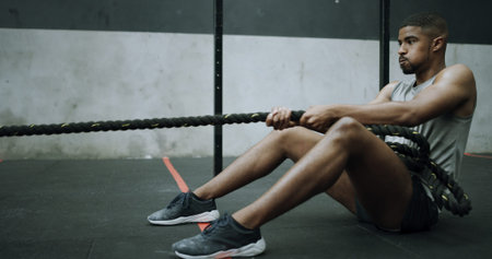 Man, battle ropes and training on gym floor with pull, intense workout and resilience with...