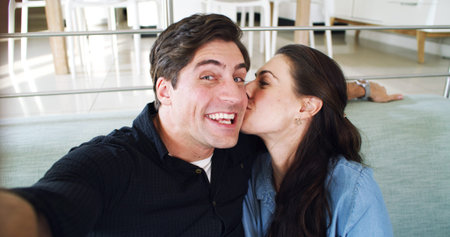 Kissing, selfie and happy couple on sofa, portrait and profile picture for memory, home and funny. Smile, man and woman on in living room, relax or photography for social media post, laughing or loveの写真素材