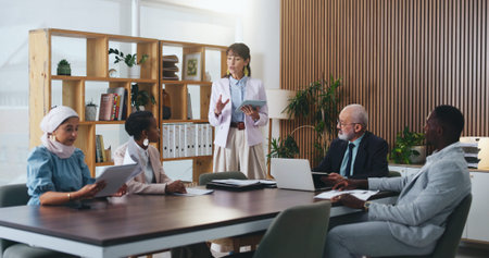Woman, tablet and review with team in office meeting on app with planning, insight or talk at...