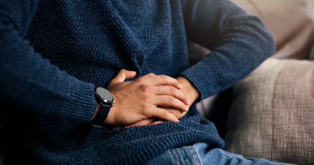 Man, hands or stomach ache with indigestion, constipation or diarrhea for pain on sofa in home....