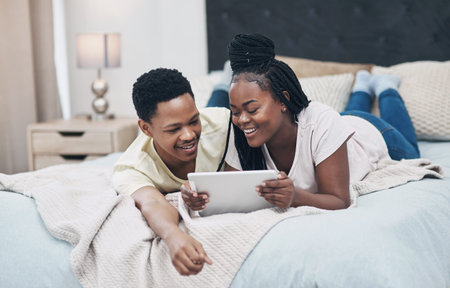 Black couple, tablet and relax on bed with smile for streaming service, movies and bonding in home. African woman, man and happy with tech, application and film choice with subscription at apartmentの写真素材