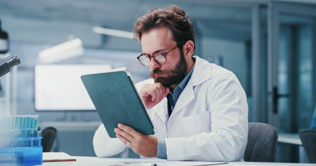 Scientist, reading or man with tablet in lab, online research paper or pathology trial study for...