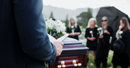 Person, hands and funeral with holy bible or coffin for memorial service, prayer or worship of god. Family, people or christianity with book, religion or faith at graveyard or cemetery for deathの写真素材